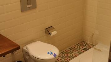 A small bathroom with a toilet, a trash can, and a shower.