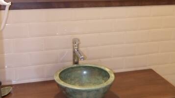 Un baño con tocador de madera, lavamanos de cerámica verde, pared con azulejos blancos y un espejo con marco verde.