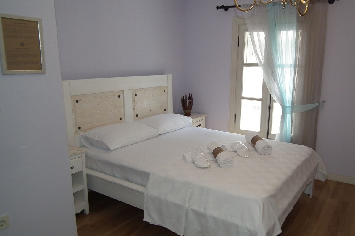 A neatly made bed with white linens and towels, a bedside table with a lamp, and a television on a stand.