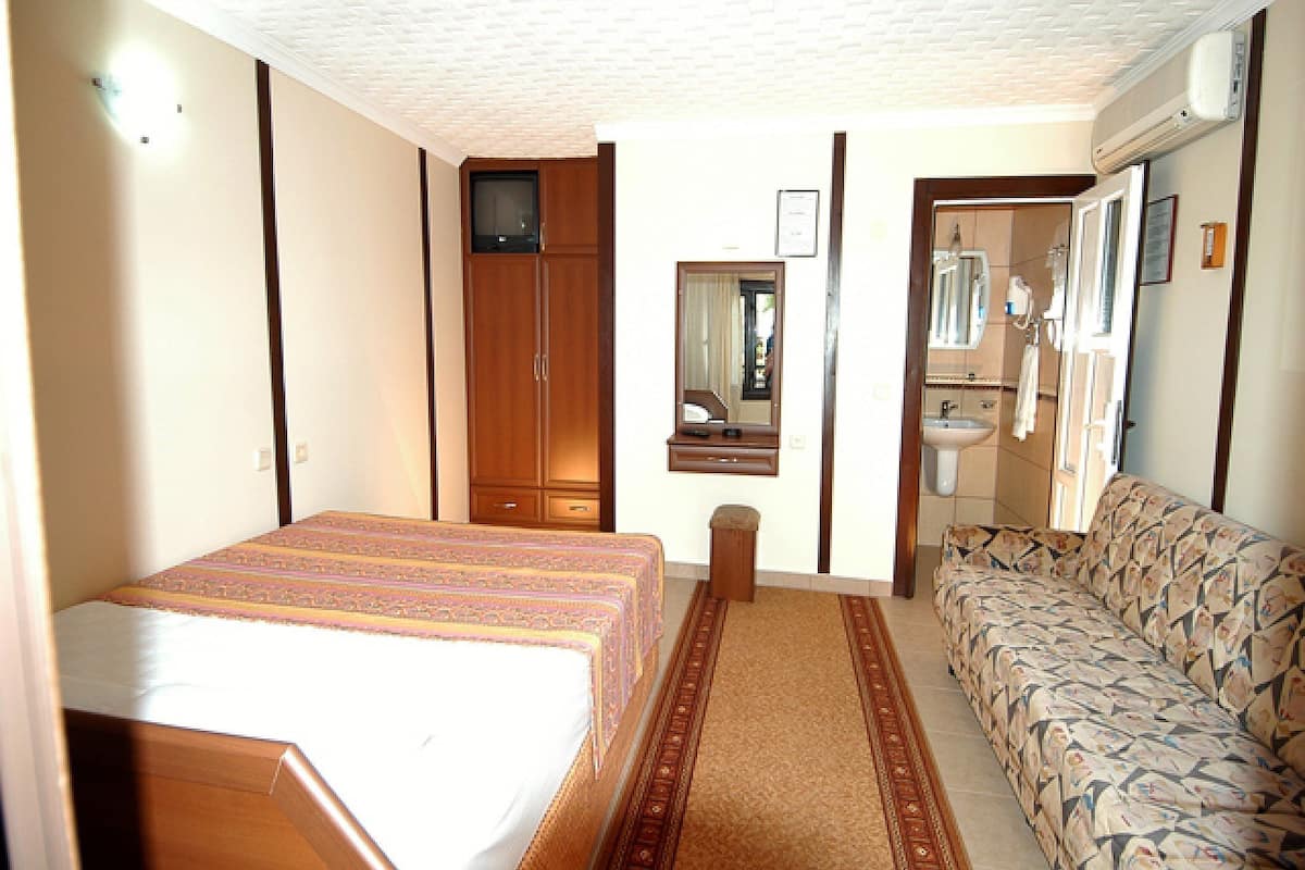 A hotel room with a bed, a sofa, a TV, a mirror, and a bathroom with a sink and mirror.