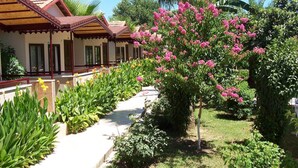 A hotel with a covered outdoor area, a garden with various plants and flowers, and a palm tree. - Hulusi Hotel (Manavgat)