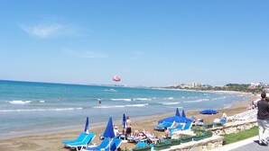 A beach with blue lounge chairs and umbrellas, a clear sky, and a distant hot air balloon. - Hulusi Hotel (Manavgat)