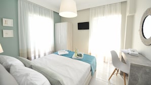 A hotel room with two beds, a desk, a chair, a TV, and a mirror. - Dionisos Elia (Nea Propontida)
