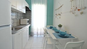 A kitchen with white cabinets, a microwave, and a dining area with blue tableware. - Dionisos Elia (Nea Propontida)