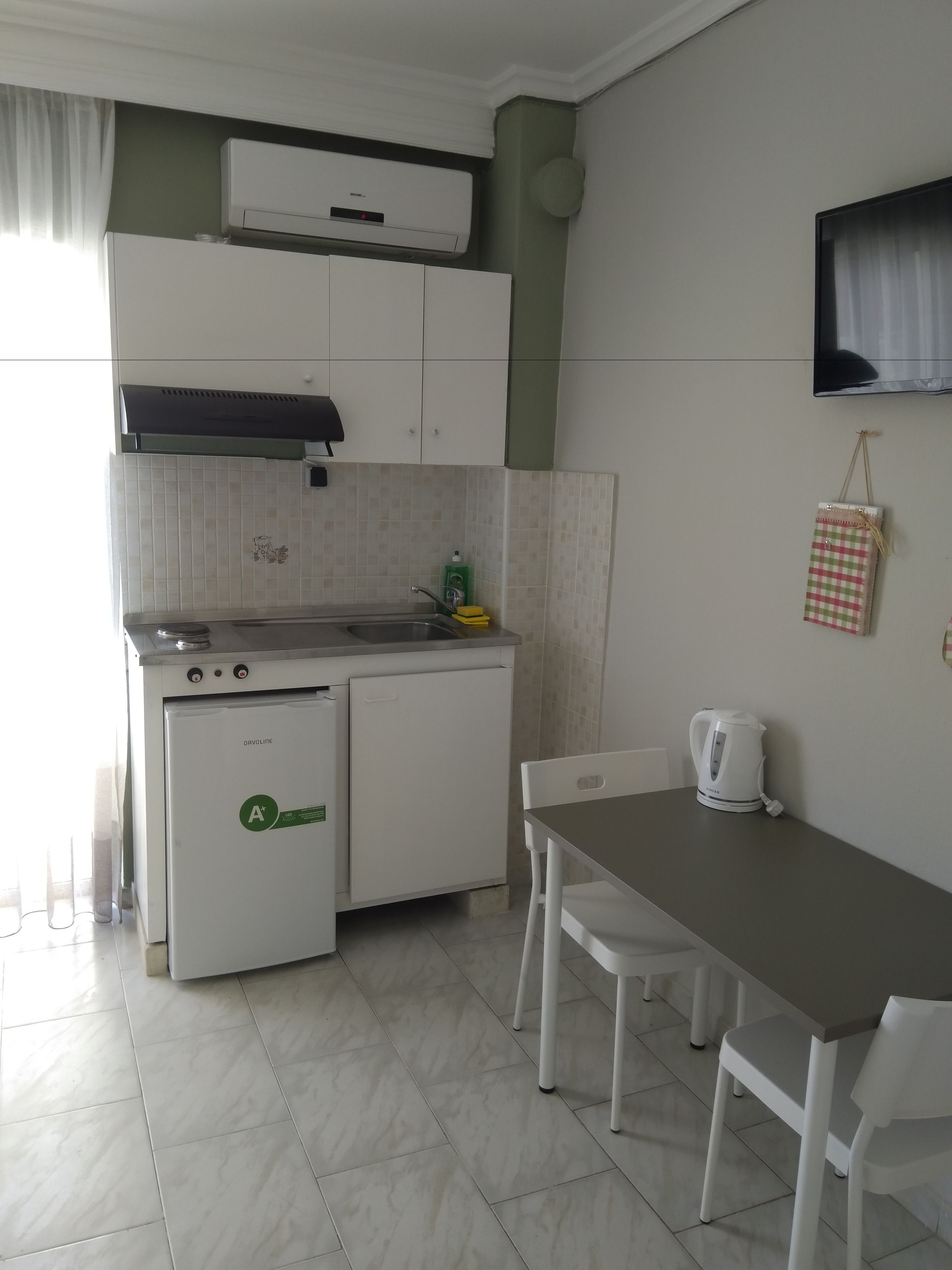 Cocina compacta con refrigerador, estufa y lavaplatos. Hay una mesa de comedor con sillas y una tetera.