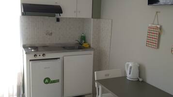 Cocina compacta con refrigerador, estufa y lavaplatos. Hay una mesa de comedor con sillas y una tetera.
