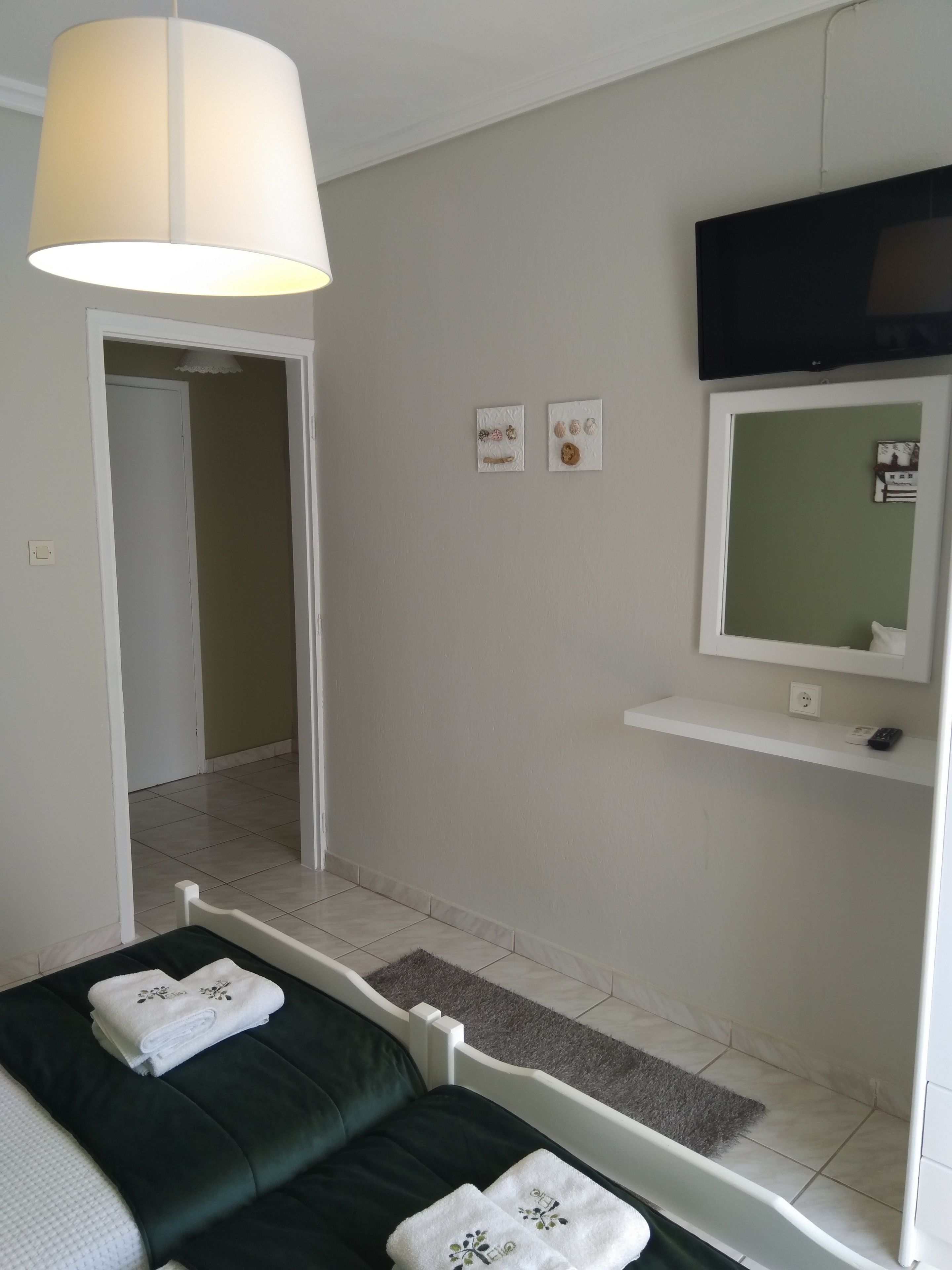 Een hotelkamer met een bed, een aan de muur bevestigde televisie, een klein plankje en een deur die naar een andere kamer leidt.