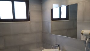 A modern bathroom with a large mirror, a sink, and a hairdryer mounted on the wall. - Dionisos Elia (Nea Propontida)
