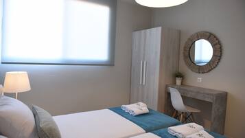 A hotel room with two beds, a desk, a chair, a mirror, and a window with blinds.
