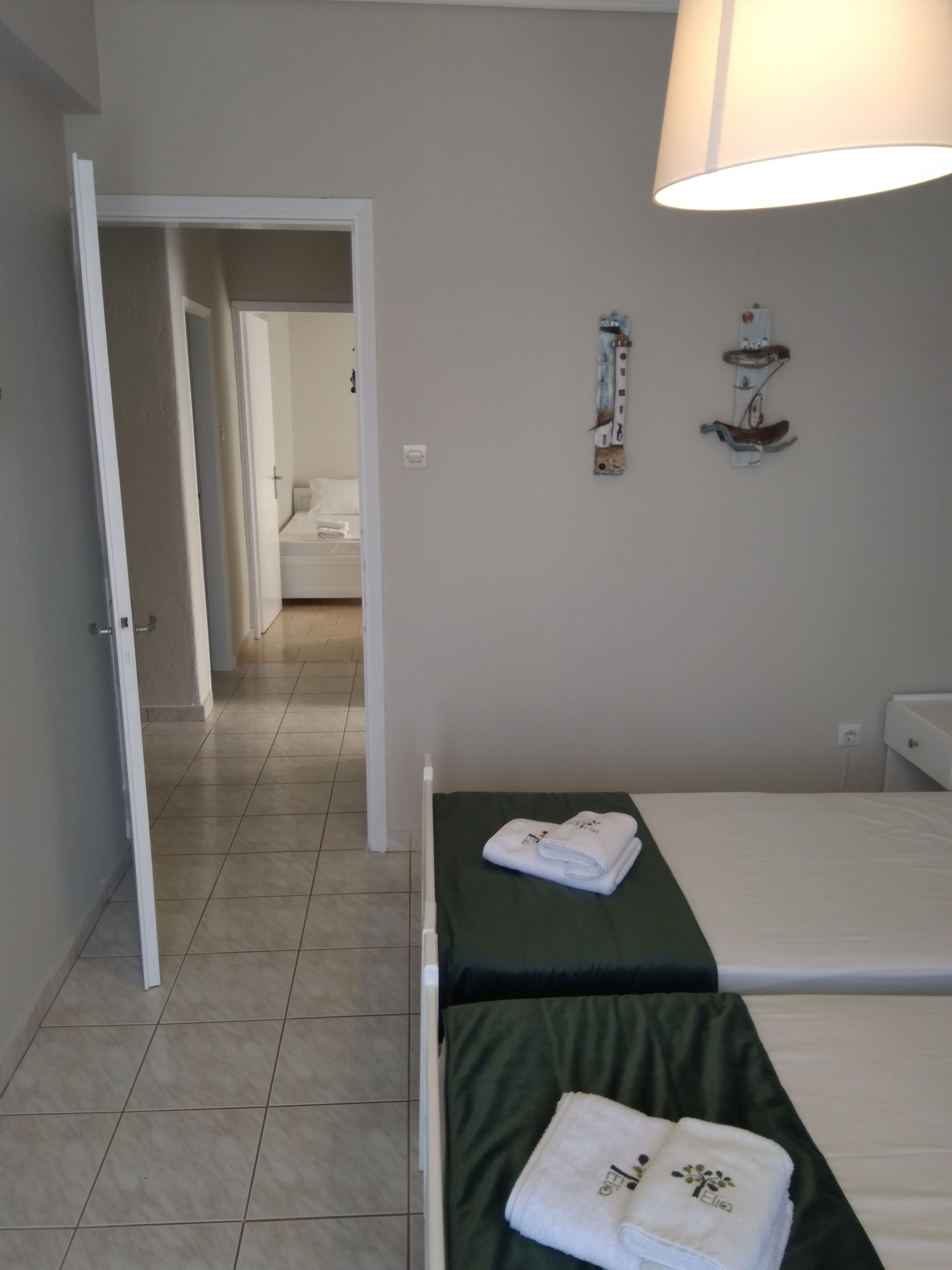 A hotel room with two beds, a bathroom, and a hallway leading to another room.