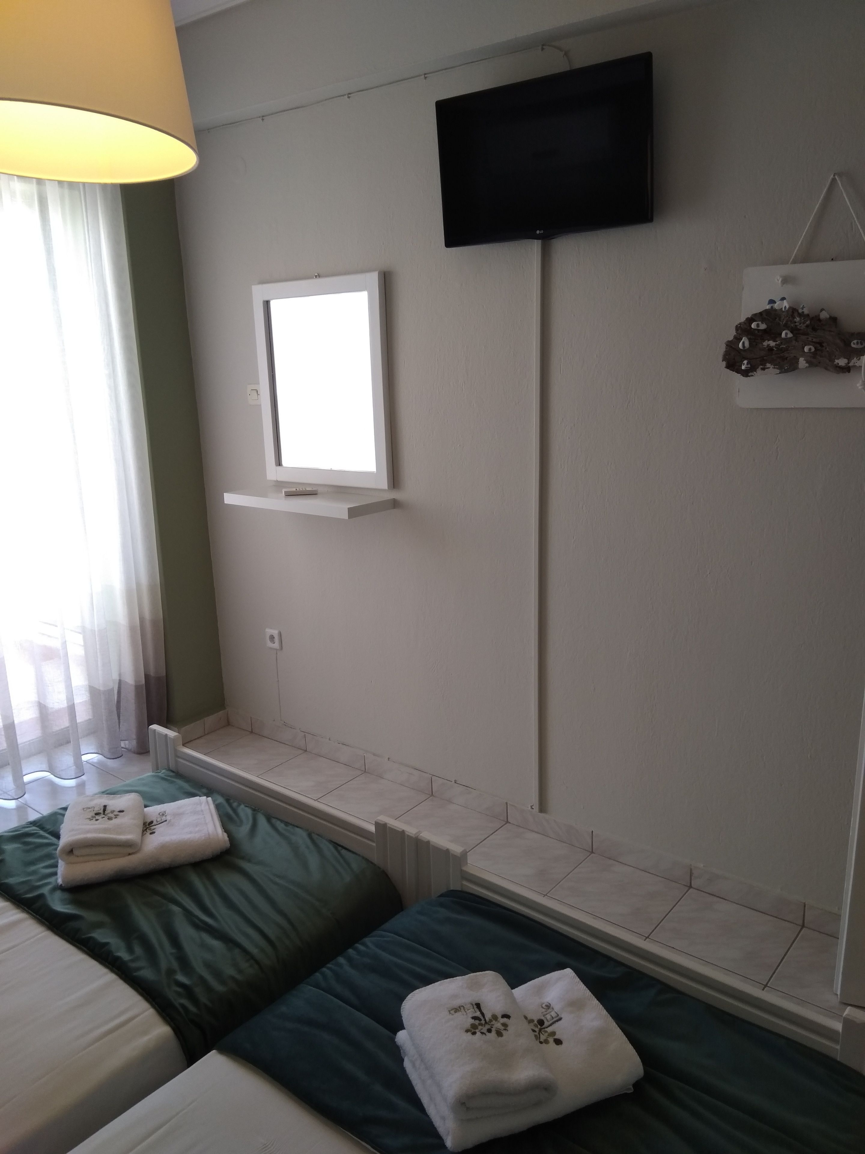 A hotel room with two beds, a TV mounted on the wall, a window with a view, and a small shelf with a decorative item.