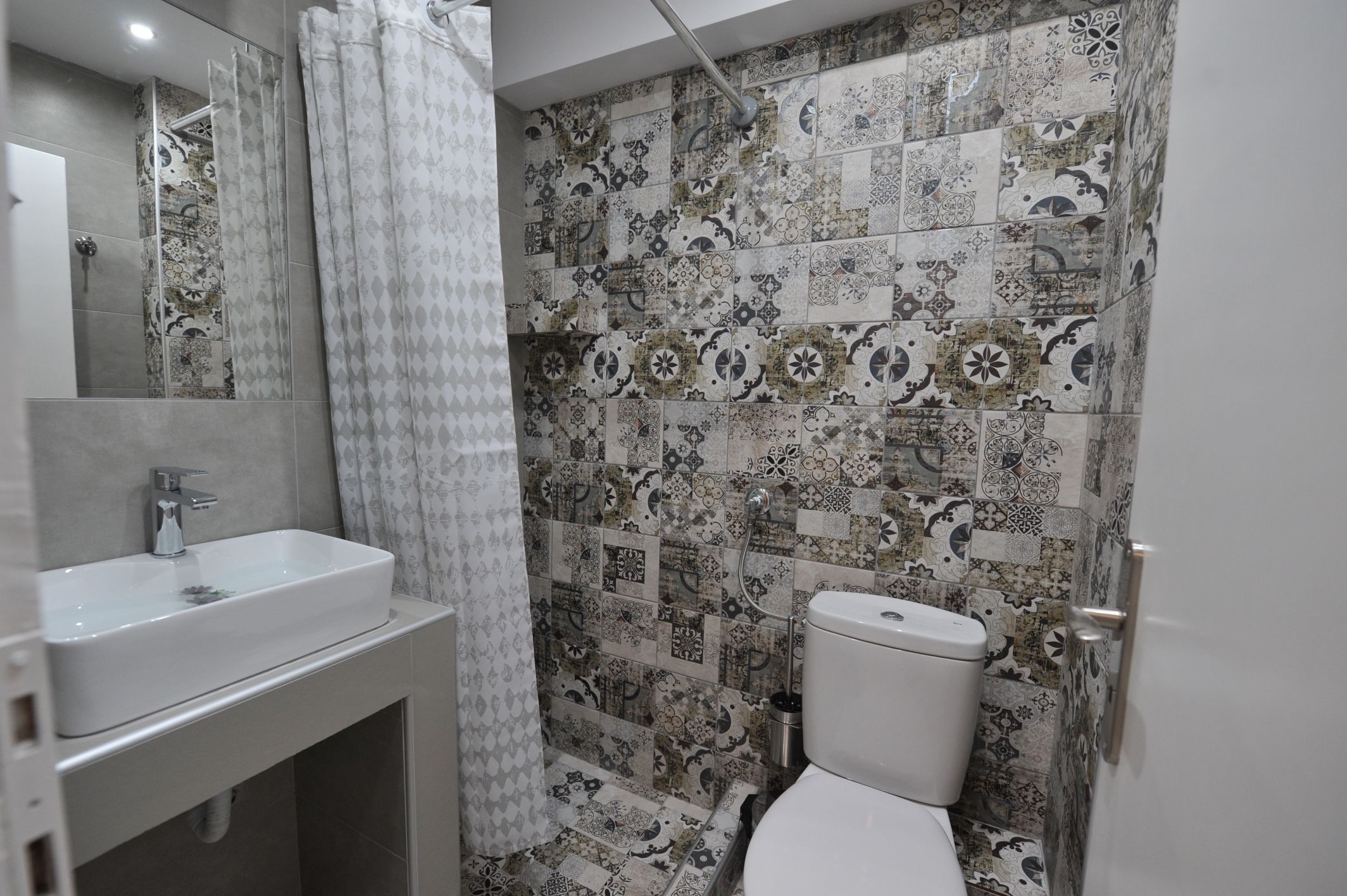A bathroom with a sink, toilet, and shower. The walls are tiled with a patterned design.