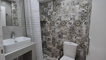 A bathroom with a sink, toilet, and shower. The walls are tiled with a patterned design.
