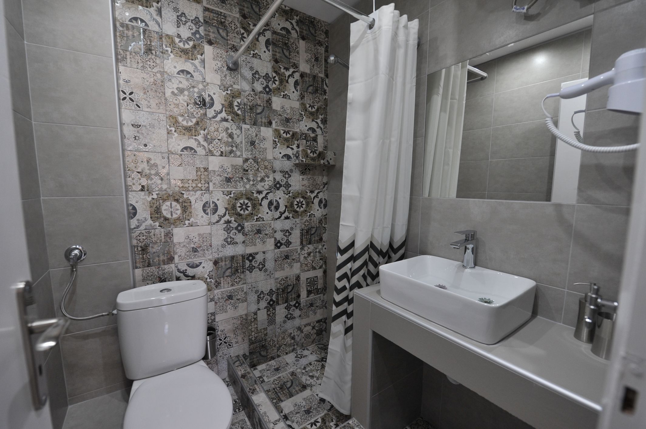 A bathroom with a patterned tile wall, a shower curtain, a toilet, a sink, and a mirror.