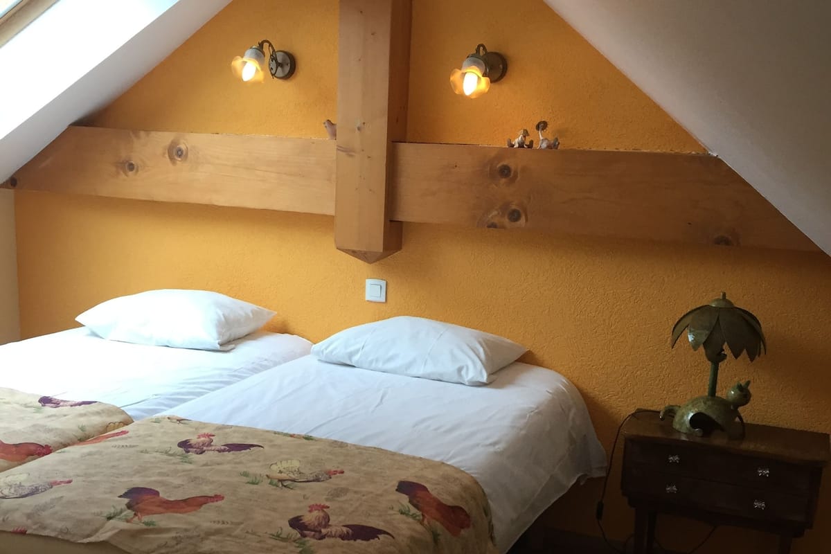Ein Schlafzimmer mit schrägen Wänden, einem Bett mit weißen Leinen, einer floralen Tagesdecke und zwei Wandleuchten.