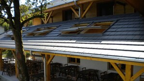 A covered outdoor seating area with tables and chairs, a tree, and a building with a sloped roof and skylights.