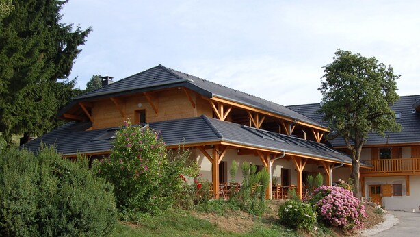 A two-story lodge with a wooden exterior, a balcony on the upper floor, and a covered outdoor seating area.