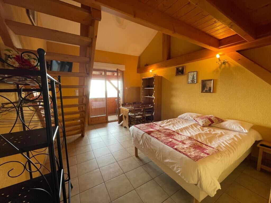 A bedroom with a bed, a desk, and a chair. There is a wooden ladder and a shelf unit.