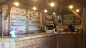 A wooden bar area with shelves of glassware and bottles, a coffee machine, and a basket.