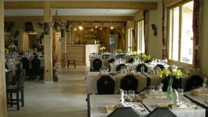 A restaurant with multiple tables set for dining, wooden beams on the ceiling, and large windows with curtains.