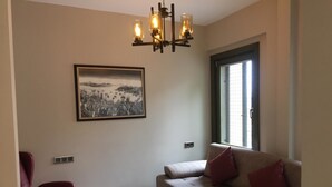A living room with a sofa, a glass coffee table, a red chair, a chandelier, and a framed picture on the wall. - Leader Mansion Hotel & Suite (Istanbul)