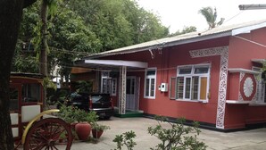 Un edificio rojo con un porche cubierto, un coche estacionado y un carruaje antiguo.