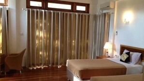 Habitación de hotel con cama, una silla, mesita de noche con lámpara y ventana con cortinas.
