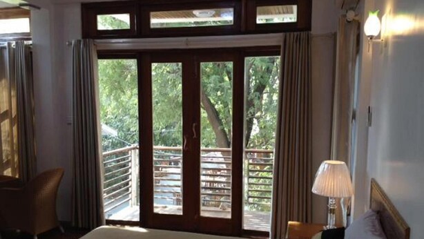 Habitación de hotel con cama, mesita de noche, lámpara y vistas al exterior a través de una puerta corrediza.