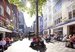 A bustling outdoor café with tables and chairs, surrounded by buildings with shops and restaurants. - Premium St Christophers Place (London)