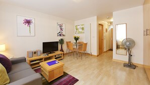 Ein modernes Wohnzimmer mit einer Couch, einem Fernseher, einem Couchtisch und einem Essbereich mit Stühlen und einem Tisch.