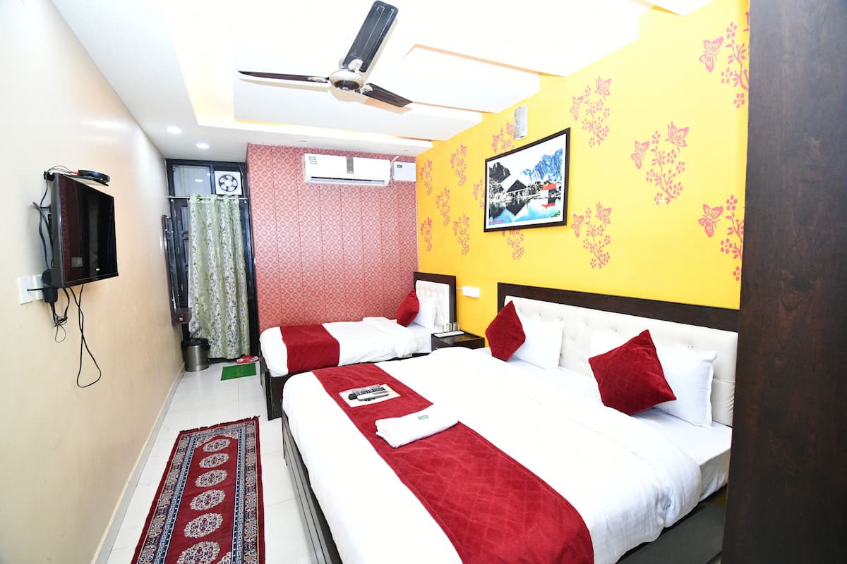 Quarto de hotel com duas camas, um ventilador de teto, ar condicionado, televisão e um tapete estampado.