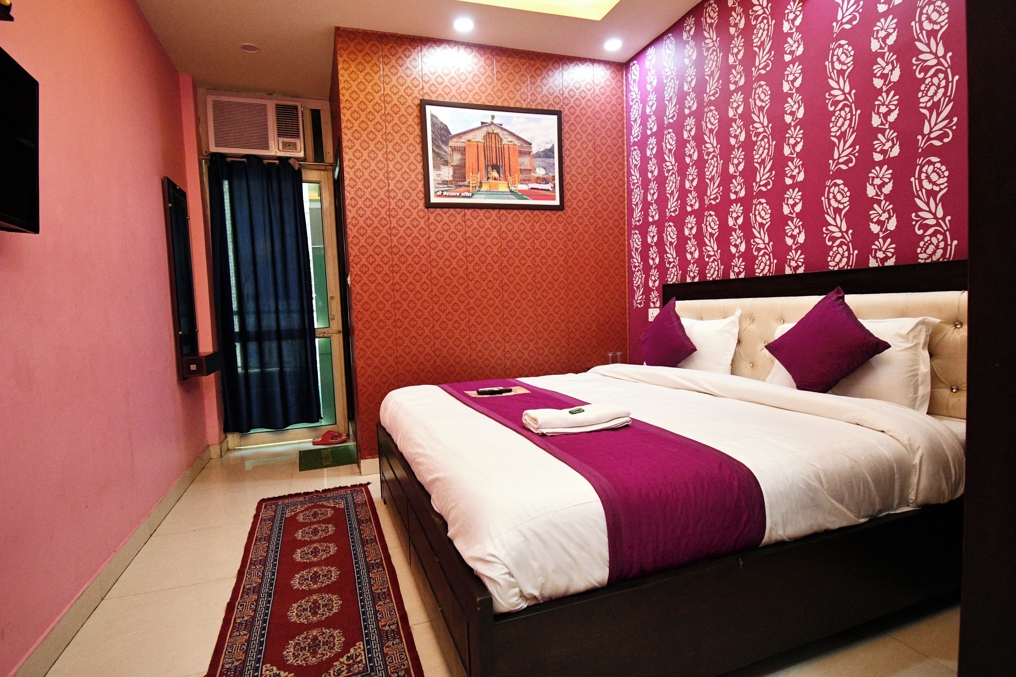 A bedroom with a large bed, a red patterned wall, a framed picture, and a red curtain.