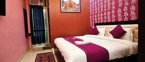 A bedroom with a large bed, a red patterned wall, a framed picture, and a red curtain.