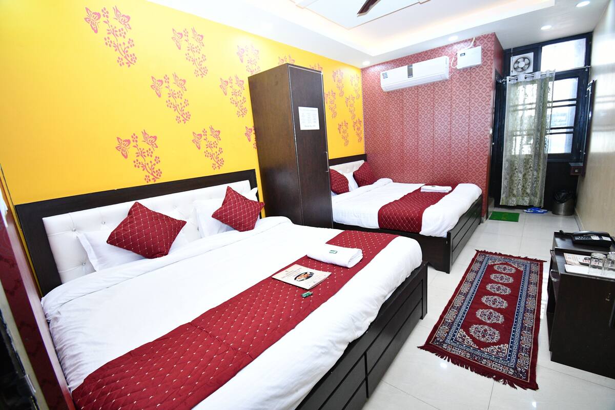 Quarto de hotel com duas camas, um guarda-roupa, uma escrivaninha e uma janela com cortinas.
