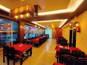 A restaurant with multiple tables and chairs, a modern ceiling design, and large windows.