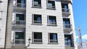 Um hotel com vários andares, varandas, um café e um carro estacionado em frente.