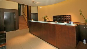 Uma área de recepção com balcão de madeira, escada e painel fixado na parede.