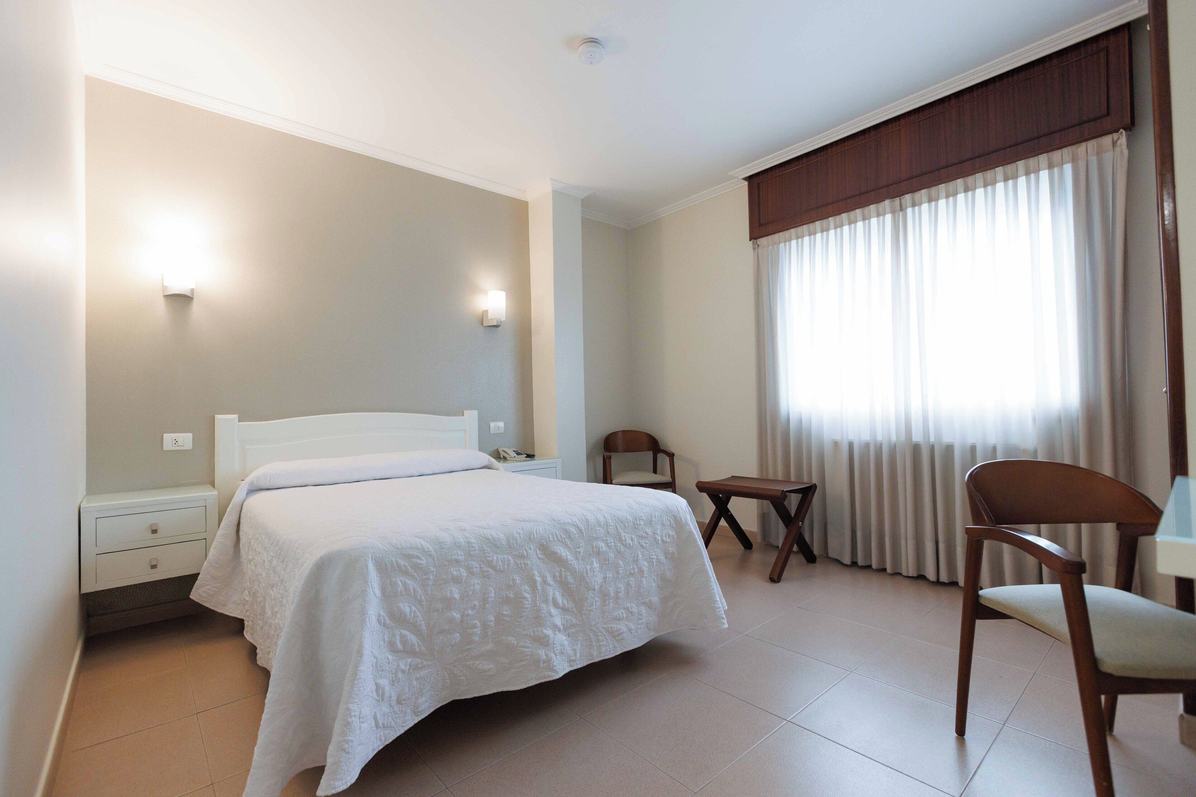 Una habitación de hotel con cama, mesita de noche, silla y una pequeña mesa.