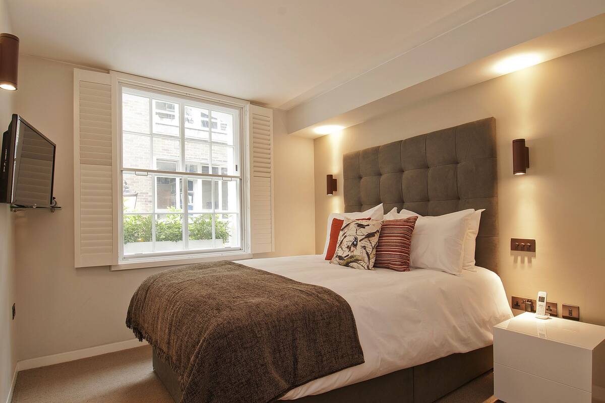 A bedroom with a large bed, a TV mounted on the wall, and a window with shutters.
