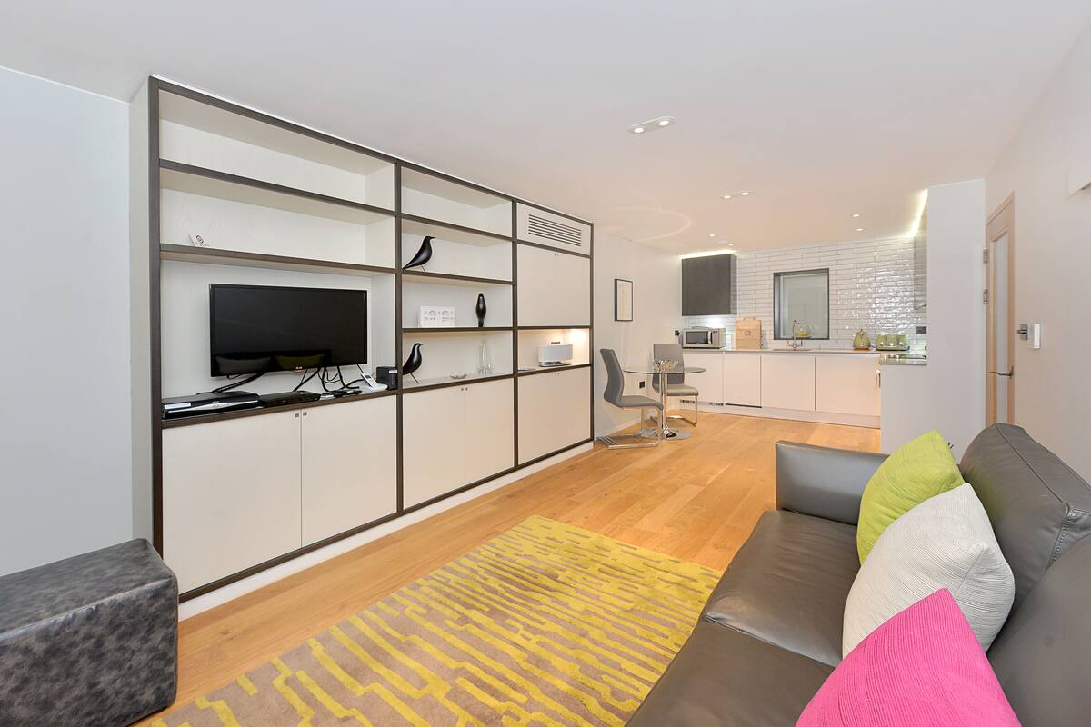 A modern living room with a sofa, a television, and a kitchen area in the background.