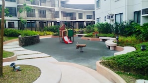 A courtyard with a playground, including a slide and swings, surrounded by greenery and modern buildings. - Bella Lifestyle Studio (Tagaytay)