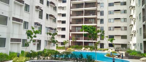 A multi-story residential building with balconies, a swimming pool, and landscaped areas.