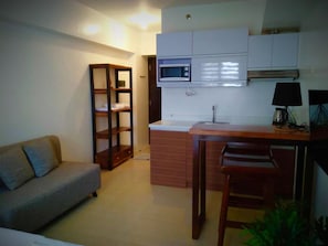 A compact kitchen with a microwave, sink, and wooden bar stools. A sofa is positioned in the living area adjacent to the kitchen. - Bella Lifestyle Studio (Tagaytay)