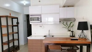 A compact kitchen with white cabinets, a microwave, a sink, and a small dining area with a wooden table and bench. - Bella Lifestyle Studio (Tagaytay)
