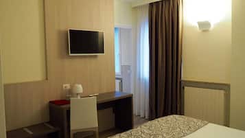 Une chambre d’hôtel avec un lit, un bureau, une chaise, une télévision et une fenêtre avec des rideaux.