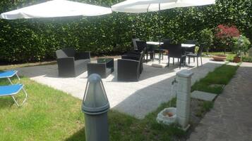 Een buitenzitplaats met tafels, stoelen, parasols en een prullenbak.