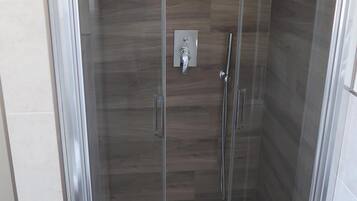 Eine Duschkabine aus Glas mit Holzboden, Bedienfeld und Handbrause.