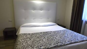 Un letto rifatto con cura, con una coperta a motivi e una testiera imbottita, e un comodino.