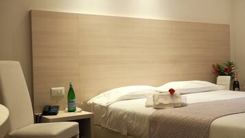 A hotel room with a bed, a bedside table with a bottle, a chair, and a telephone.