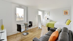 A modern, well-lit room with a dining area, a sofa, a bed, and a window with a city view. - Camden Serviced Apartments by Globe (London)